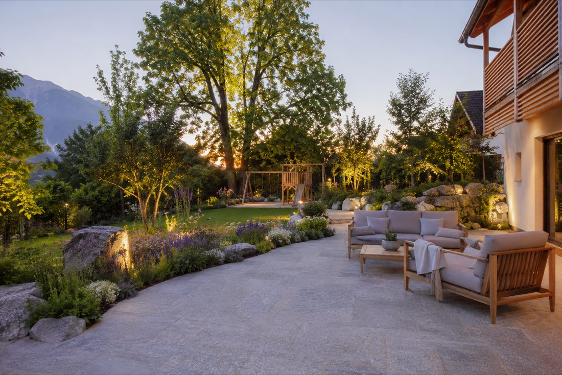Naturnahe Gartenterrasse mit Steinplatten, Felsen und Bergblick in der Abendsonne